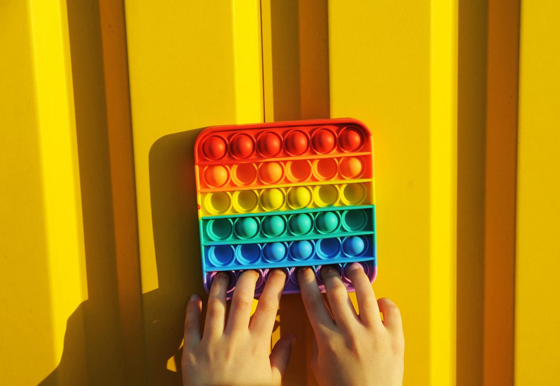 Anti stress rainbow hand toy on yellow background. Push pop fidget toy. Girl plays in pop it. Anti stress hand toy.